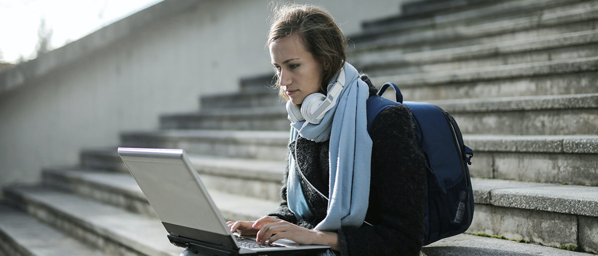 Junge Frau sitzt auf einer Treppe mit einem Laptop auf dem Schoß.