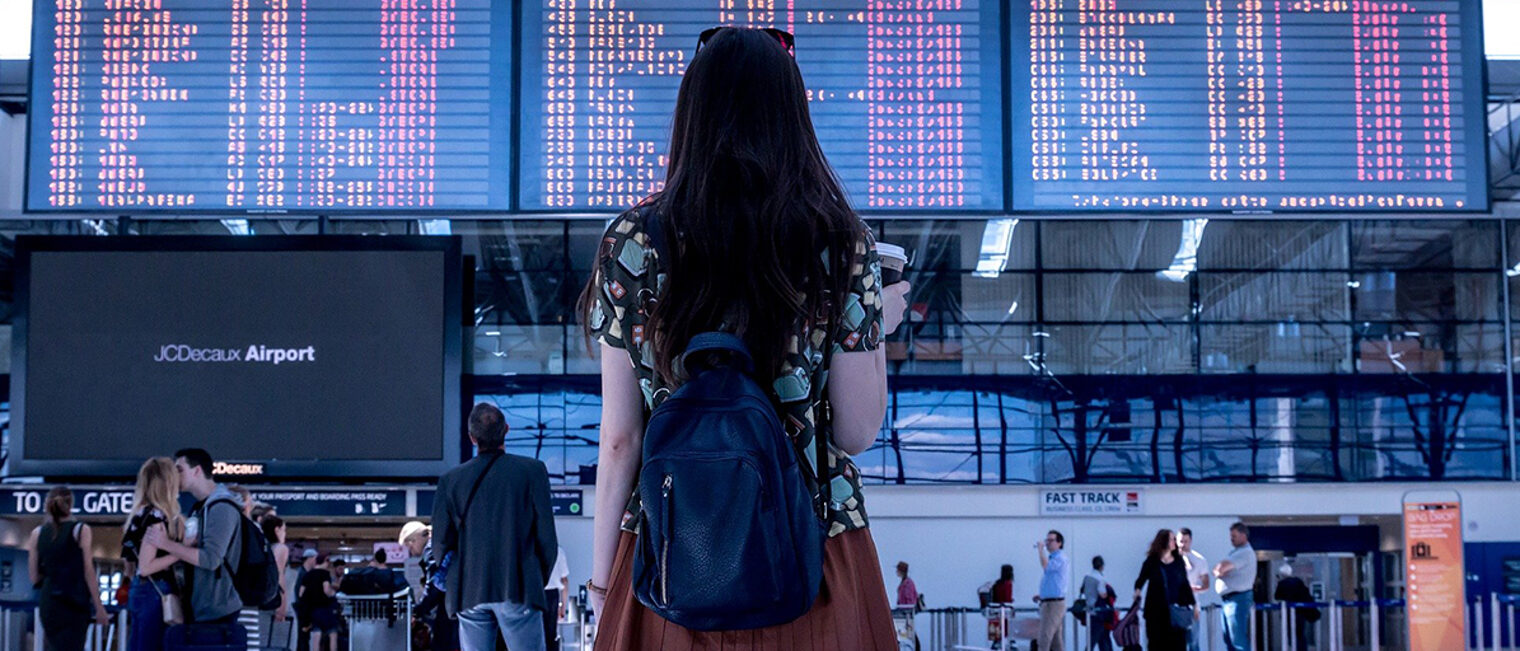 Junge Frau steht auf einem Flughafen vor einer Übersichtstafel.